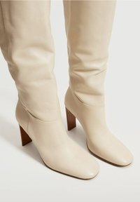 Bottes beige hauteur genou en cuir lisse avec un bout carré et un talon bloc, dotées d'une tige ajustée et de détails de couture minimaux.