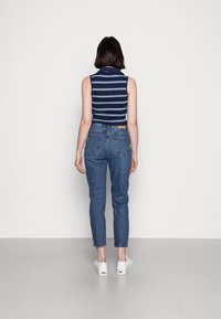 Marinblå-randig ärmlös topp, hög krage, kombinerad med ljusblå denimjeans och vita sneakers. Snygga linjer, figursydd silhuett, avslappnad stil.