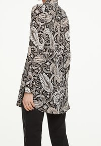 Black and white paisley pattern shirt with long sleeves, high collar, side slits, and a relaxed fit, made from lightweight fabric.