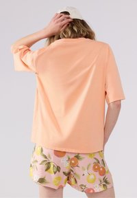  ferskenfarvet bomulds t-shirt med afslappet pasform og korte ærmer, parret med lyserøde shorts med et citrusfrugtprint og grønne blade.
