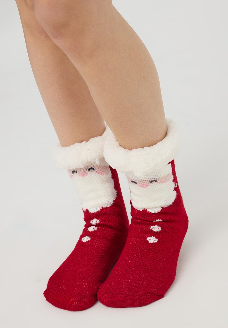 Czerwone, puszyste skarpetki z białym, pluszowym mankietem. Na przedniej części znajduje się wzór twarzy Świętego Mikołaja, a po bokach dodano białe kropki jako akcenty.