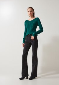 Green cable-knit sweater with V-neck and long sleeves paired with black flared jeans and black heeled boots, minimalistic design.