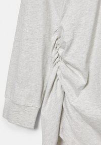 Vêtement gris clair à manches longues avec un détail de tissu froncé et plissé sur le côté et une manche avec poignet.