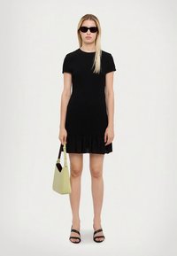 Crna haljina s kratkim rukavima i naboranim rubom, uparena sa svijetlo zelenom torbicom i crnim sandalama. Glatka tekstura, ležeran dizajn.