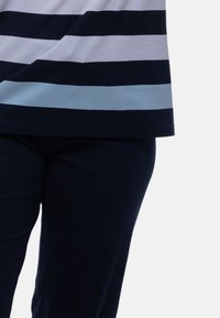 Raidallinen puuvillapaita, jossa on vaaleanharmaita, tummansinisiä ja vaaleansinisiä vaakaraitoja, yhdistettyyn tummansinisiin housuihin. Pehmeä materiaali, rento istuvuus.