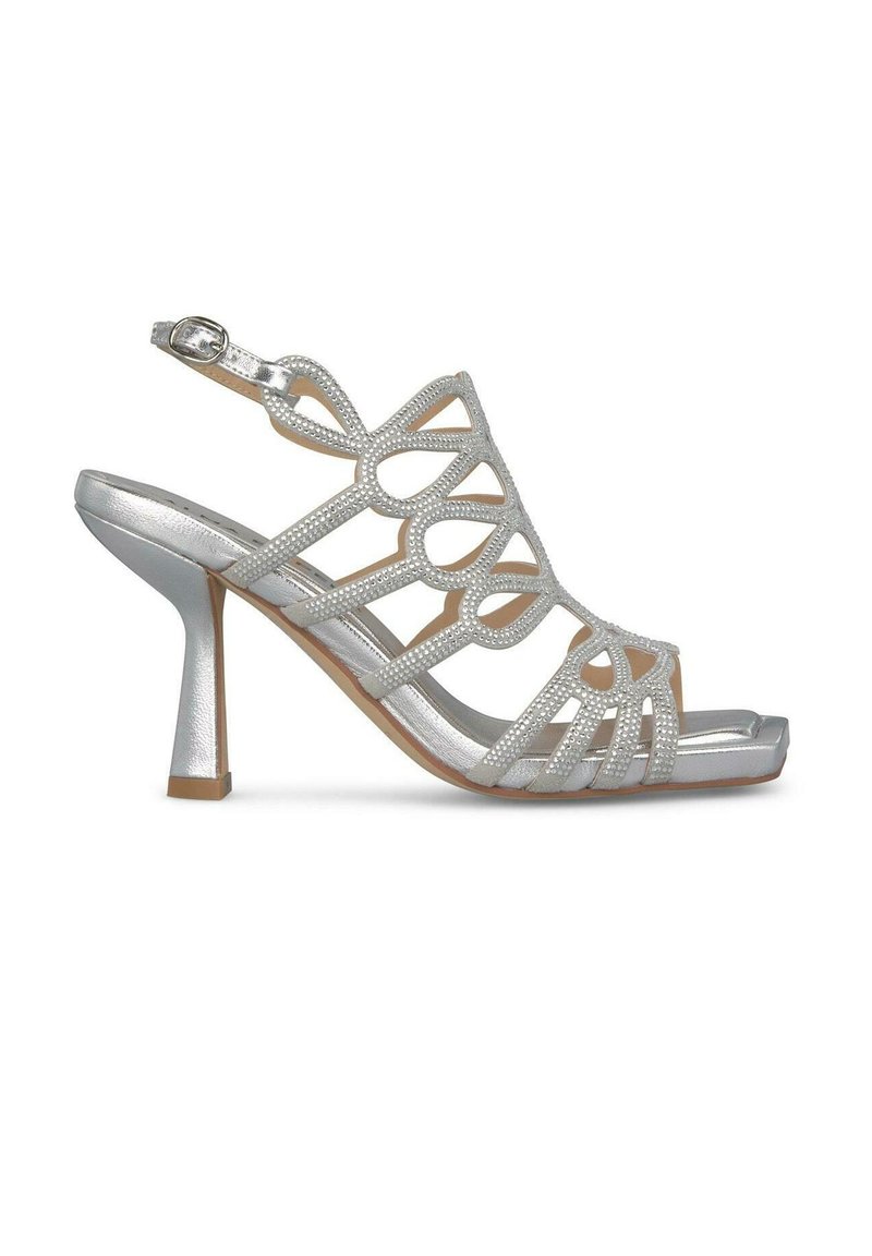 Srebrne wysokie sandały na obcasie z wyciętymi wzorami i akcentami z cyrkonii. Posiadają pasek na kostkę i kwadratowy czubek. Błyszczące wykończenie dodaje kontrastu.