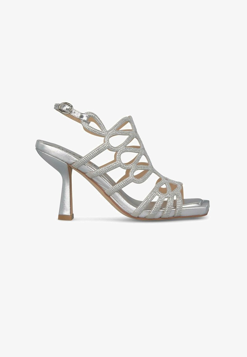 Srebrne wysokie sandały na obcasie z wyciętymi wzorami i akcentami z cyrkonii. Posiadają pasek na kostkę i kwadratowy czubek. Błyszczące wykończenie dodaje kontrastu.