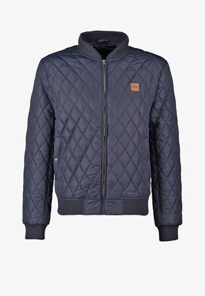 Tumesinine tikitud bomber-jakk ribitud krae ja mansettidega, millel on ees lukuga kinnitamine ja väike silt rinnal.