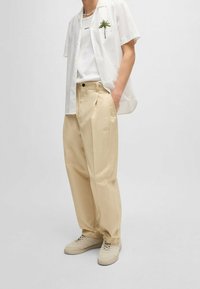 Lichtgewicht witte, korte mouwen overhemd met palmprint over een effen witte tanktop, gecombineerd met beige geplooide broek en lichtgekleurde sneakers.