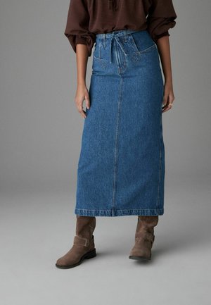 Denim maxi skirt in light blue with a high waist, drawstring detail, and front seam. Worn with brown ankle boots. Smooth texture.