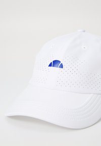 Gorra blanca con diseño perforado, logotipo azul en la parte frontal, visera curva y ojales para ventilación. Textura de tela suave.