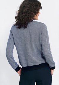 Granatowa i biała bomberka w deseń w jodełkę z prążkowanymi mankietami i dołem. Miękka textura, luźny krój i lekko skrócony fason.