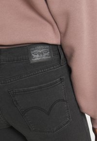 Jeans de mezclilla negra con una etiqueta de parche de cuero que presenta 'Levi Strauss & Co.' y un patrón de costura distintivo en el bolsillo trasero.