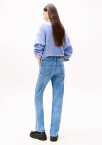 Jeans in denim azzurro chiaro con una vestibilità comoda, vita su misura e due tasche posteriori, abbinati a un morbido maglione blu. Scarpe nere con zeppa.