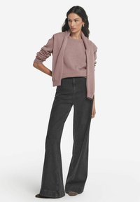 Jasnoróżowy sweter nałożony na dopasowaną bluzkę, w zestawie z czarnymi spódnicami dzwonowymi z wysokim stanem. Podkreślone miękkie tekstury i minimalistyczne akcenty.