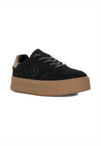 Sneaker nera in suede con una spessa suola in gomma marrone. Presenta lacci neri, un logo a stella e un accento beige sul tallone.