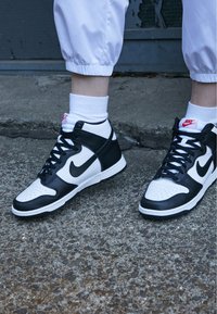 Sneaker alte in pelle nera e bianca, con punta perforata, lacci neri e dettagli del logo Nike rossi sulla linguetta.