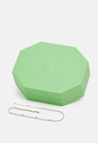 Zelená octagonálna šperkovnica s textúrovaným povrchom, vedľa nej leží jemný strieborný náramok s ružovými akcentmi.