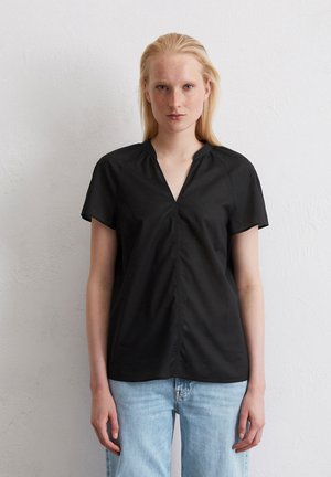 Zwarte blouse met korte mouwen en een V-halslijn, met een geplooide voorkant en een gladde textuur. Gepaard met lichtblauwe spijkerbroek.