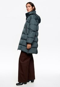 Ocieplana ciemnoszara kurtka z kapturem, kieszeniami na zamek i puchatym fasonem. Połączona z szerokimi brązowymi spodniami i czarnymi botkami na obcasie.