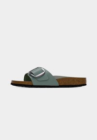 Πράσινο σανδάλι slide με φαρδύ λουράκι, ασημένια πόρπη και φελού ποδόμακτρο· μαύρη ανάγλυφη ελαστική σόλα για πρόσφυση.