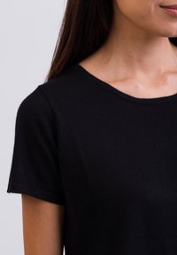 Sort kortærmet T-shirt med rund halsudskæring. Stoffet ser blødt og lidt tekstureret ud, hvilket fremhæver et enkelt og klassisk design.