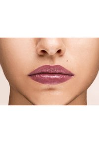 Matte mauve lippenstift aangebracht op volle lippen met subtiele textuurdetails, tegen een zachte, neutrale huidachtergrond.