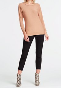 Maglione beige a maniche lunghe con scollatura a barca, caratterizzato da dettagli con bottoni sulle maniche, abbinato a pantaloni neri skinny e stivaletti alla caviglia con motivo a serpente.