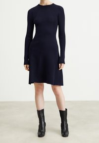 Granatowa dzianinowa sukienka z długimi rękawami, prążkowanym wzorem, okrągłym dekoltem i rozszerzanym dołem; w połączeniu z czarnymi skórzanymi botkami do kostki.