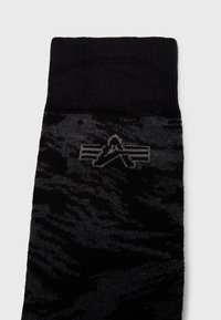 Calcetines negros con un puño acanalado, que presentan un patrón texturizado en gris oscuro y un diseño sutil de logo en gris en un costado.