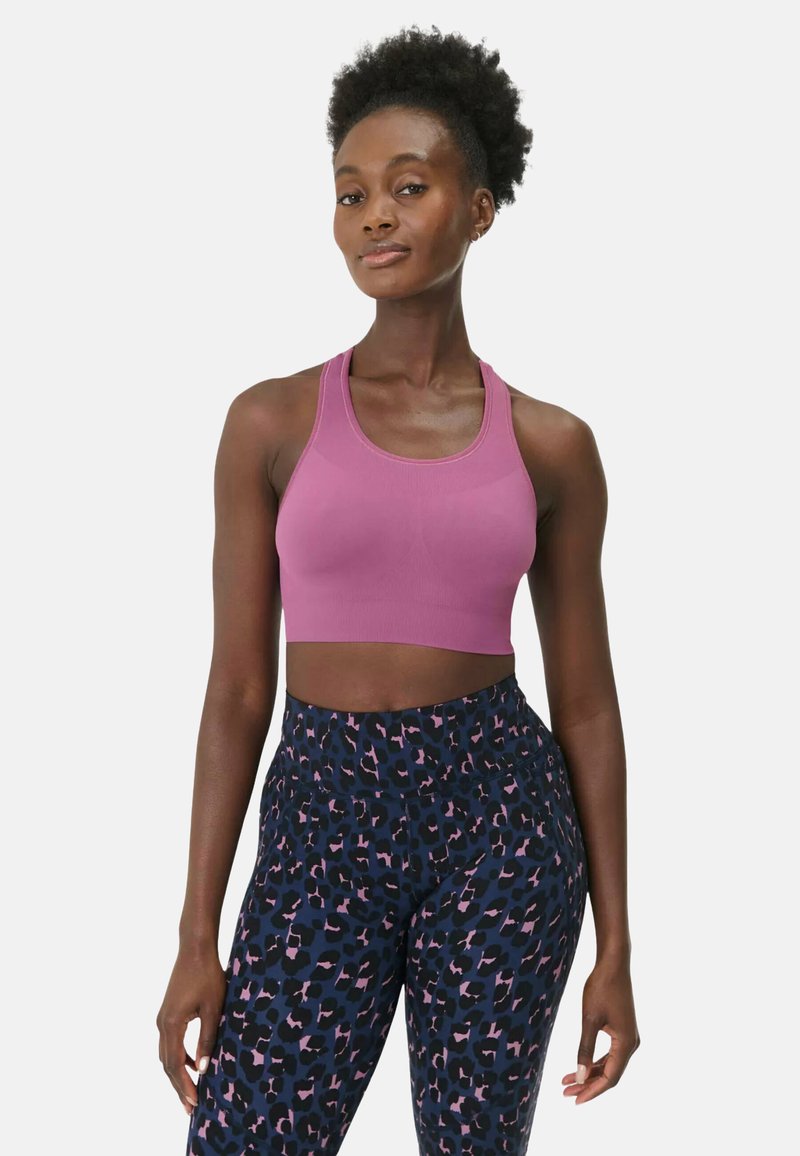 Femme portant un crop top rose sans manches et des leggings taille haute noirs avec imprimé léopard rose et bleu, debout devant un fond blanc.