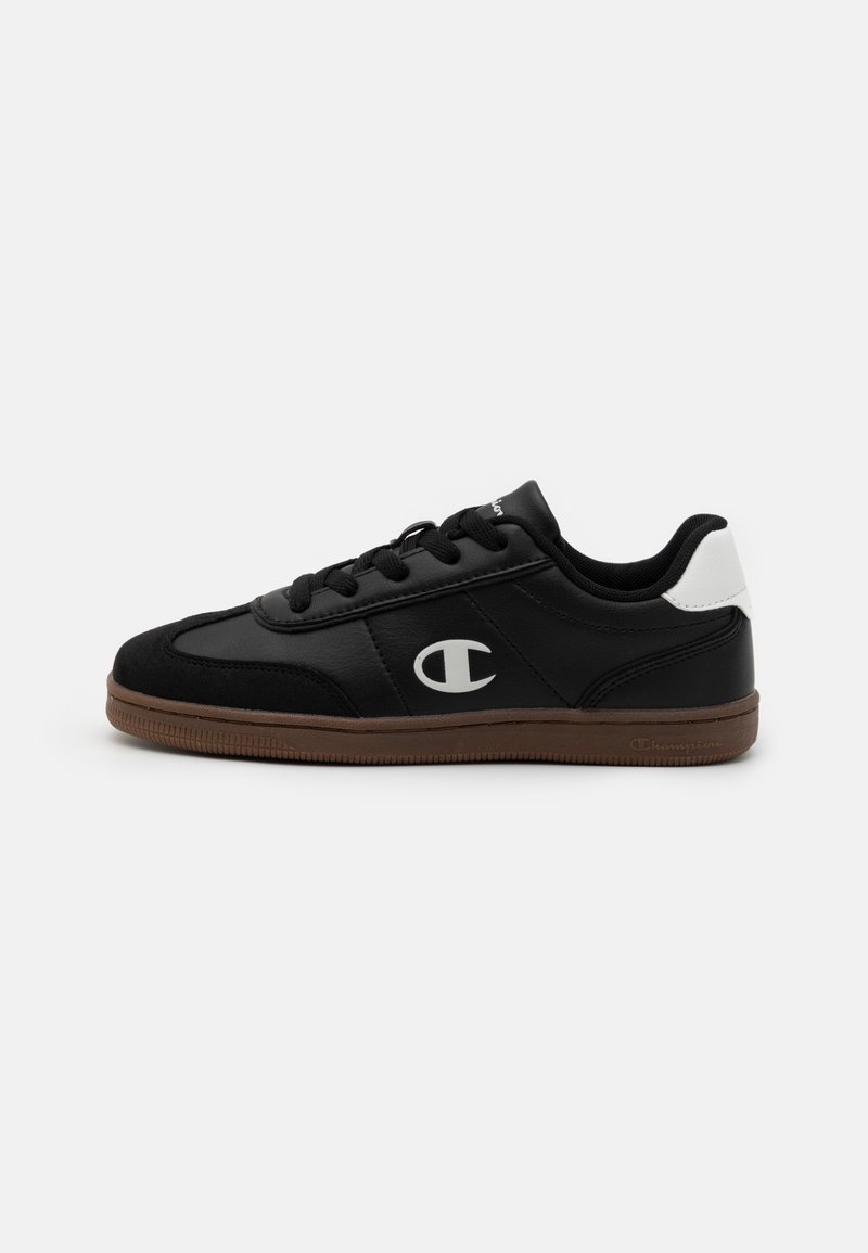 Sorte atletiske sneakers med en glatt skinnøvre, semskede detaljer, hvit hæl, svarte snøringer og såle i brun gummi. Har en logo på siden.
