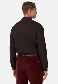 Mörkbrun texturerad långärmad polo skjorta ihop med vinröda kordbyxor och ett flätat brunt bälte. Enkel design utan mönster.