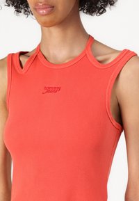 Roter gerippter Tanktop mit ausgeschnittenen Schulterdetails und gesticktem "Tommy Jeans"-Logo auf der Brust. Weicher, taillierter Stoff.