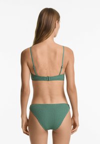 Zeleni teksturirani bikini set s prilagodljivim naramenicama i kopčanjem bralettea, u paru s usklađenim niskim donjim dijelom.