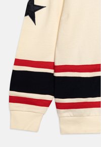 Polsino del maglione in cotone color crema con strisce nere, rosse e crema. Presenta un motivo a stella nera sulla parte superiore. Tessuto morbido.