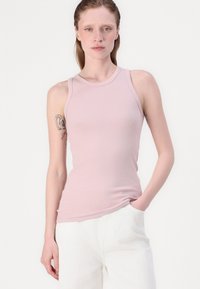 Débardeur sans manches rose clair avec un design ajusté et une texture côtelée. Doté d'un col rond et d'un ourlet incurvé, associé à un pantalon blanc.
