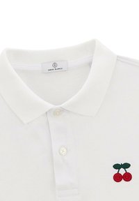Witte polo met een gestructureerde kraag. Heeft rode geborduurde kersen met groene bladeren. Knopsluiting aan de voorkant en een textuur stof.
