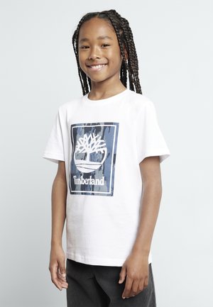 Witte katoenen t-shirt met een blauw en grijs grafisch ontwerp van een boomlogo en de tekst "Timberland" gedrukt op de voorkant. Korte mouwen.