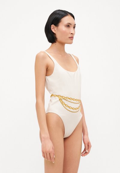 Maillot de bain blanc à encolure dégagée, avec une ceinture en chaîne dorée en accent. La texture lisse et la coupe ajustée mettent en avant un style minimaliste.