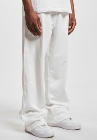 Hvide sweatpants lavet af blød bomuld, med et afslappet fit, sidelommer og enkle sømdetaljer, parret med hvide sneakers.