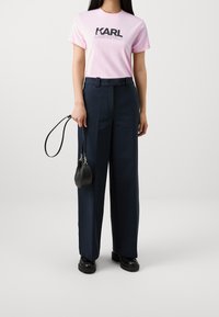 Camiseta de algodón de color rosa claro con la impresión "KARL LAGERFELD", combinada con pantalones de vestir navy de pierna ancha y un bolso negro pequeño. Zapatos negros.