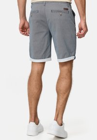 Gray woven shorts with a textured pattern, cuffed hem, and two back pockets featuring button closures. White sneakers complement the outfit.