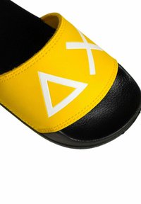 Infradito gialli con suola nera texturizzata. Presentano forme geometriche bianche sulla fascia gialla, bordi cuciti e una finitura liscia.