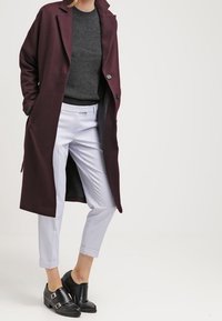 Bordowy długi płaszcz na szarym swetrze, w połączeniu z jasnoniebieskimi spodniami  ciętymi i czarnymi butami na klamrę. Gładki materiał z dopasowanym krojem.