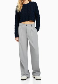 Granatowy krótki sweter z grubym splotem, zestawiony z jasnoszarymi spodniami o szerokich nogawkach. Spodnie mają zapięcie na guziki i delikatne zakładki.