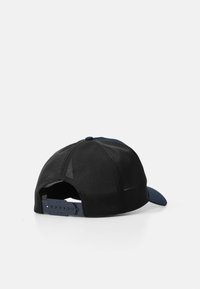 Melna un zila cepure ar izliekto vizieri, sietu aizmuguri, regulējama siksna un gludu tekstūru. Aizmugurējā siksnā ir logo.