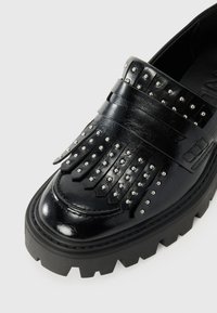 Black leather loafer featuring studded fringe detail, a chunky black sole, and a glossy finish, highlighting texture and design.