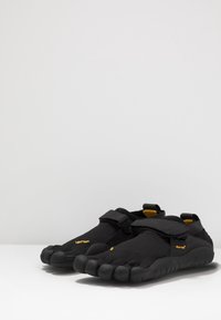 Chaussures noires à cinq orteils avec une sangle Velcro. Fabriquées en mesh et en caoutchouc, elles disposent d'une semelle texturée et d'un marquage Vibram. Design léger et flexible.