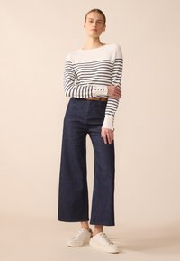 Top à manches longues rayé blanc et marine avec des poignets à boutons, associé à un pantalon en denim bleu foncé à jambes larges et des baskets blanches.